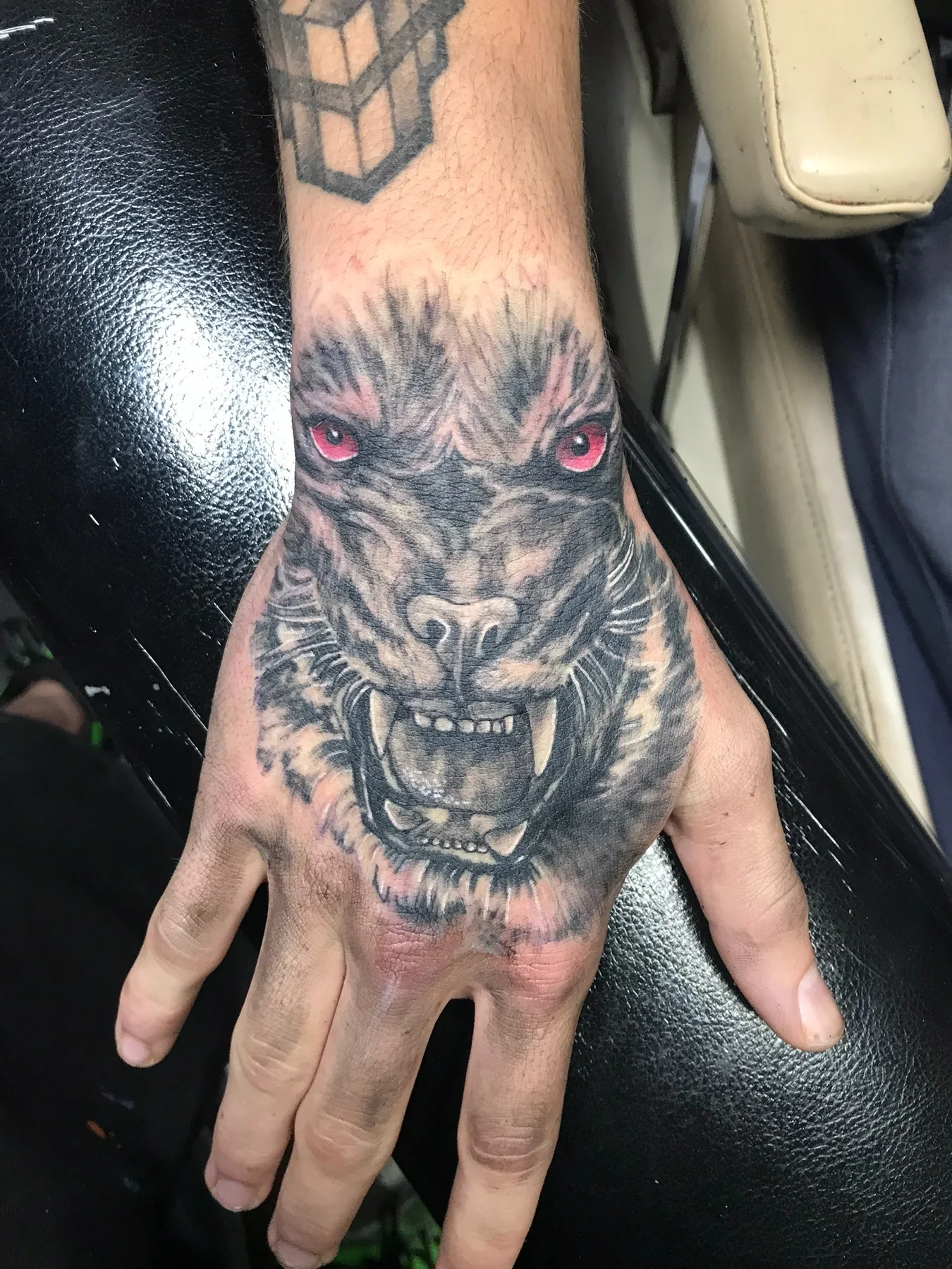 Black-and-gray snarling wolf hand tattoo with red eyes by Josh Poindexter